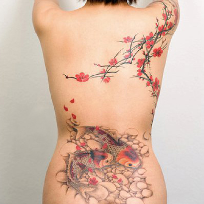 Woman's back with tattoo of cherry blossoms and fish.